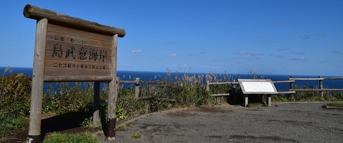 A wooden sign with Japanese text, a wooden fence, and a view of the ocean.