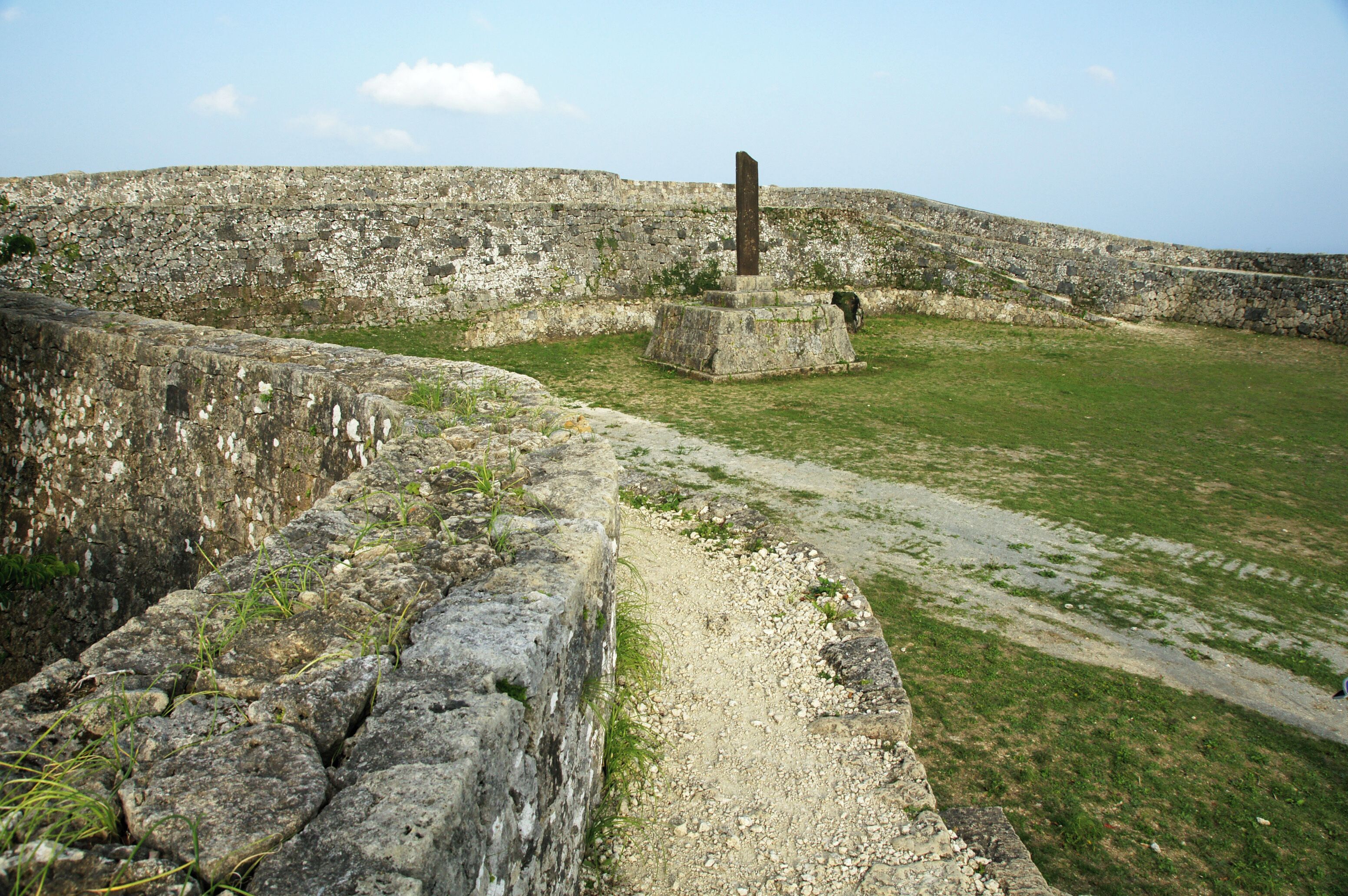 A stone fortification with a central pillar, a grassy field, and a stone wall.