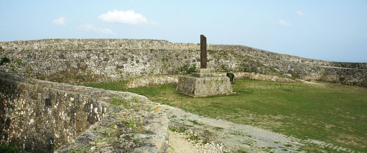 A stone fortification with a central pillar, a grassy field, and a stone wall.