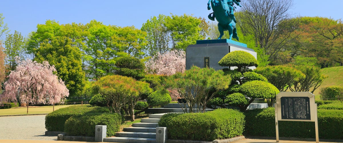 A statue of a mounted figure on a pedestal in a park with neatly trimmed bushes and trees.