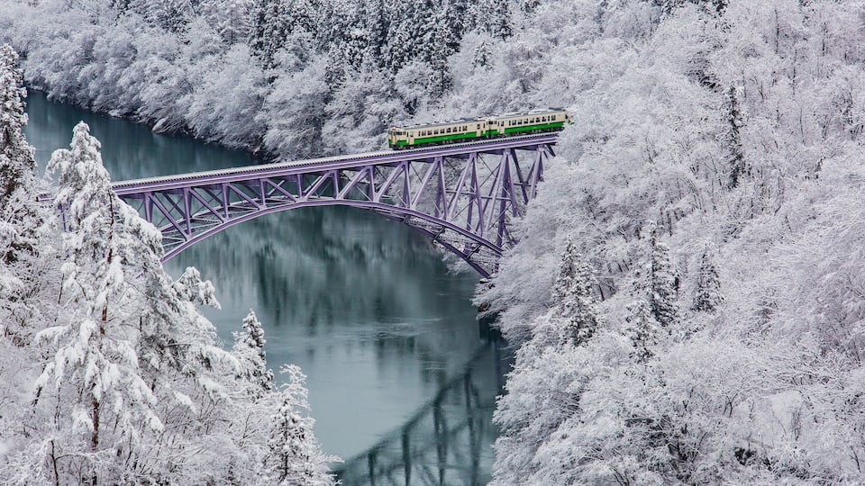A train on a bridge over a river surrounded by snow-covered trees.