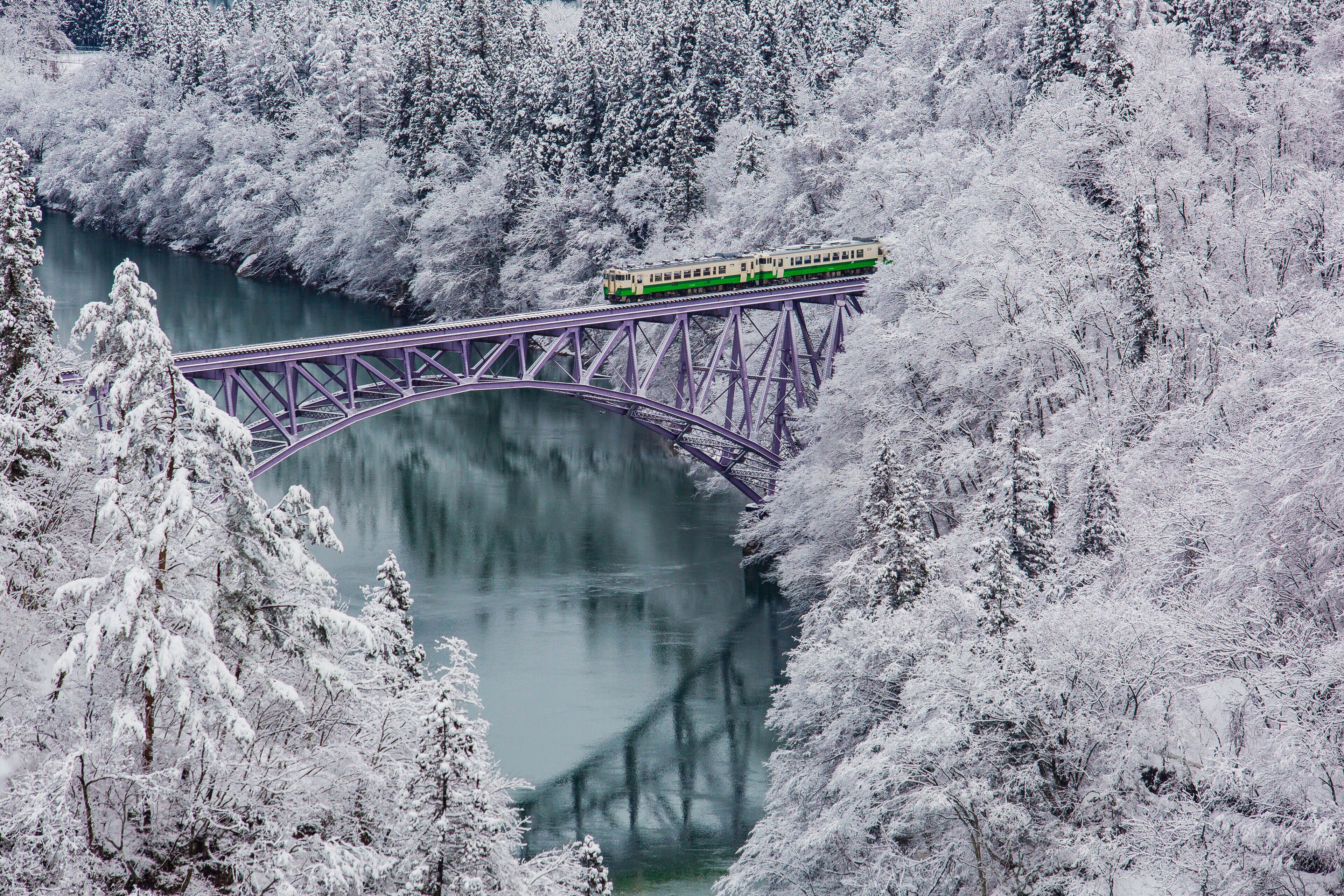 A train on a bridge over a river surrounded by snow-covered trees.