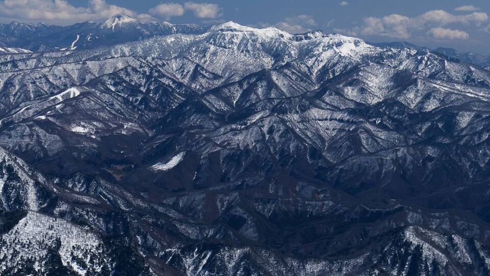 A snow-covered mountain range with rugged terrain and distant peaks under a clear sky.