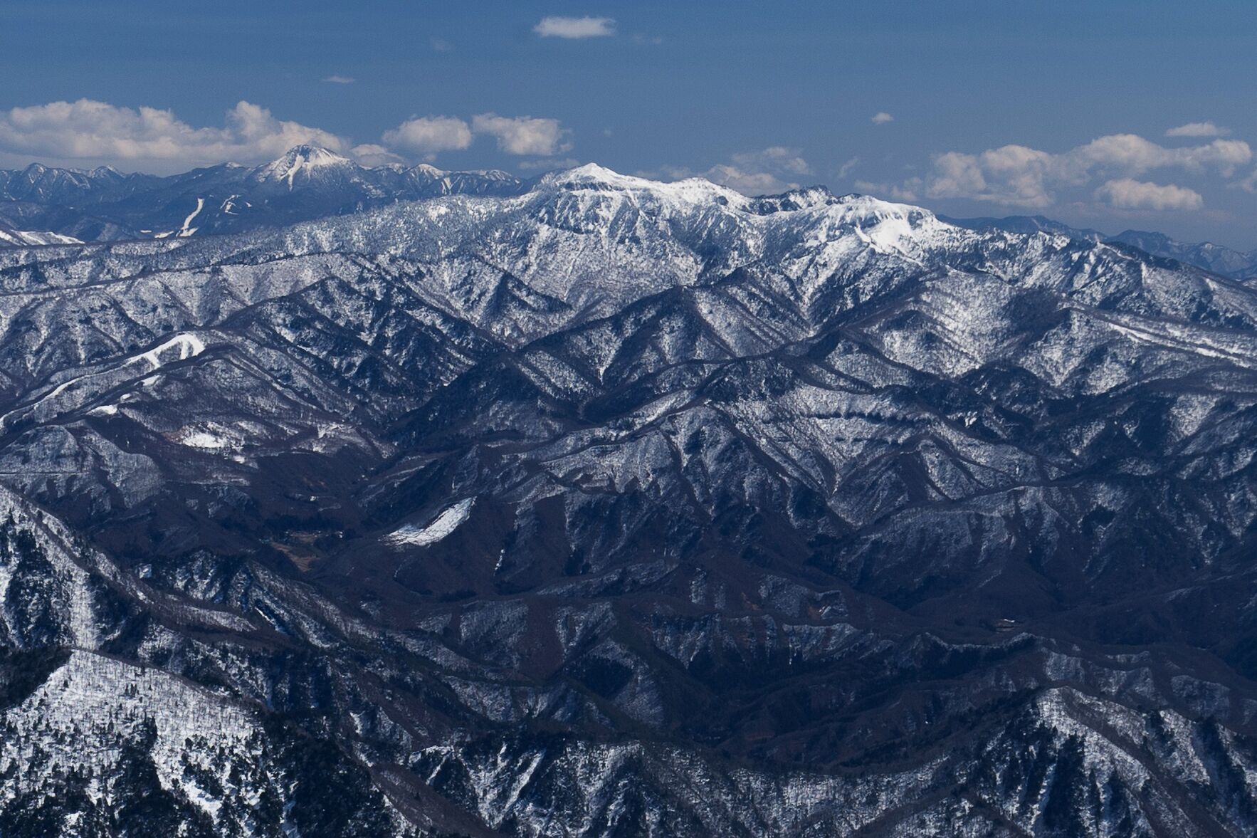 A snow-covered mountain range with rugged terrain and distant peaks under a clear sky.