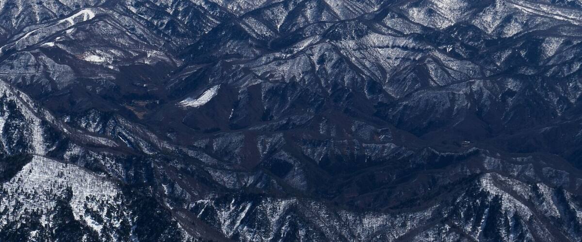 A snow-covered mountain range with rugged terrain and distant peaks under a clear sky.