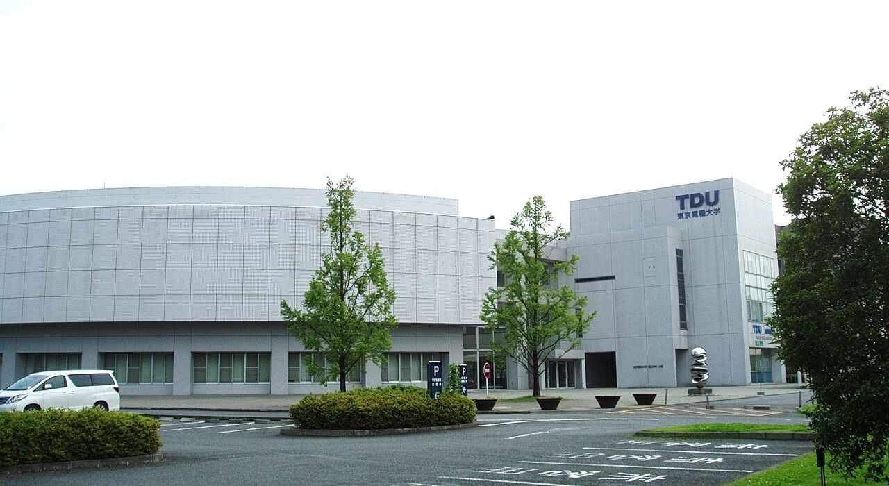 A modern building with the letters "TDU" on the facade, surrounded by trees and a parking lot.