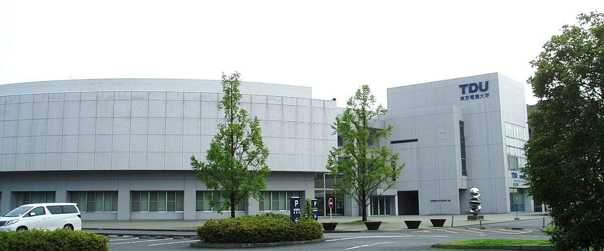 A modern building with the letters "TDU" on the facade, surrounded by trees and a parking lot.