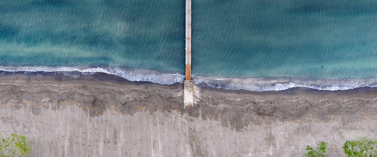 A coastal landscape with a concrete pier extending into the ocean.