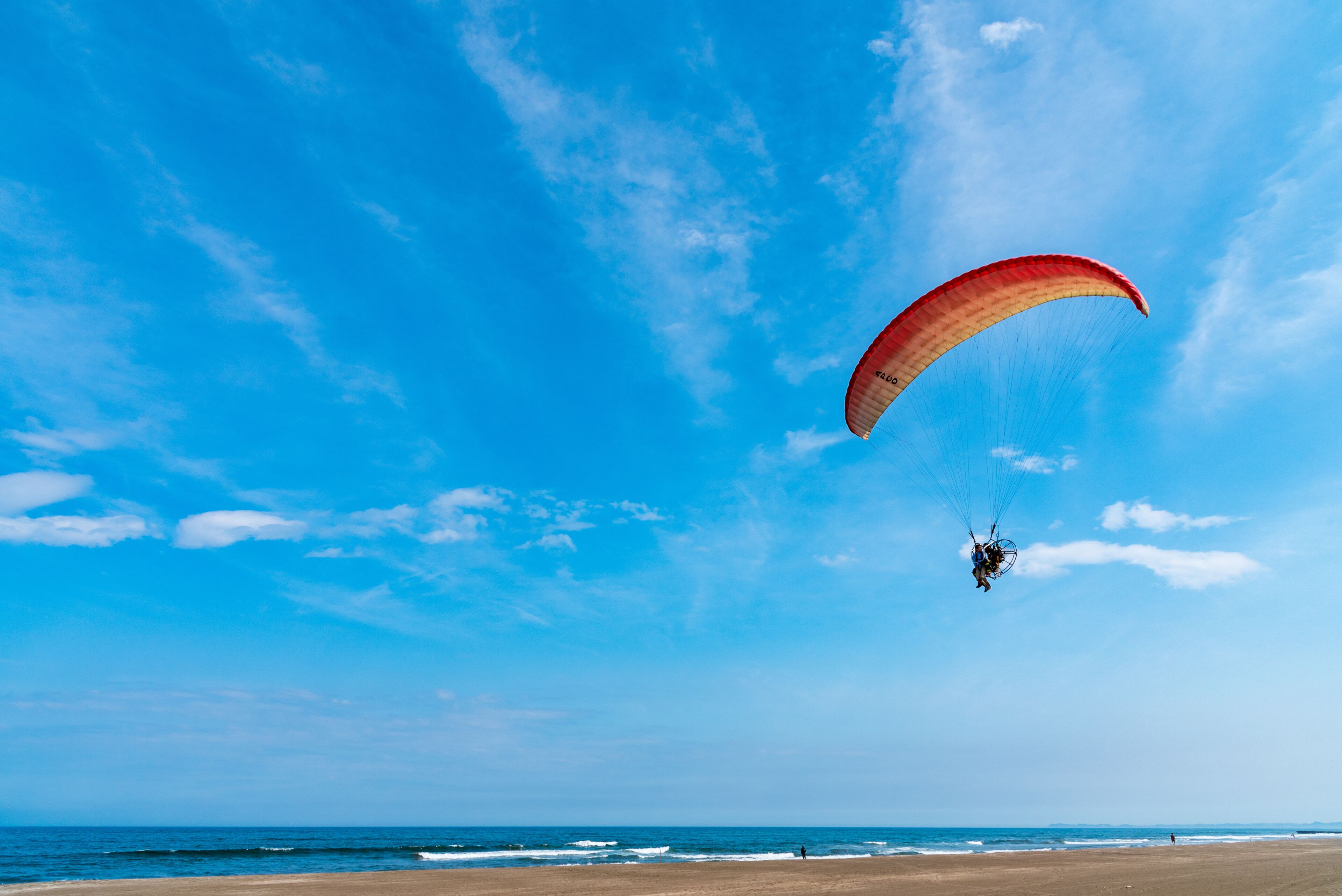 A person paragliding over a beach with clear skies.