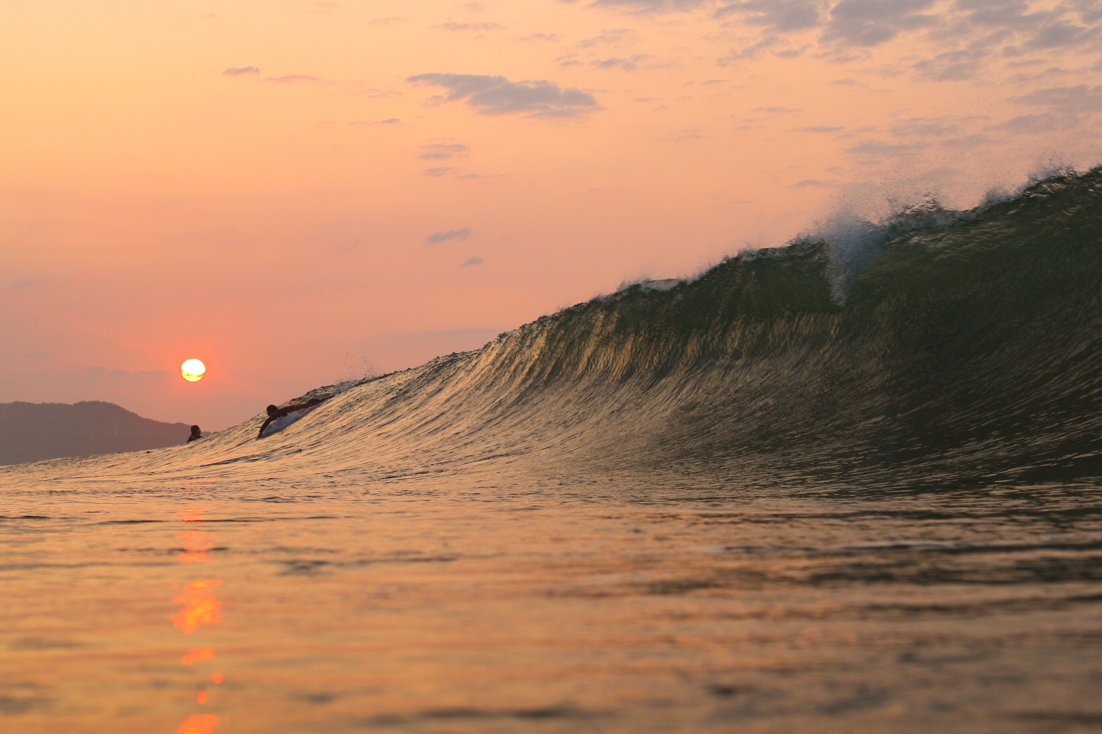 A large wave with a surfer riding it during sunset.
