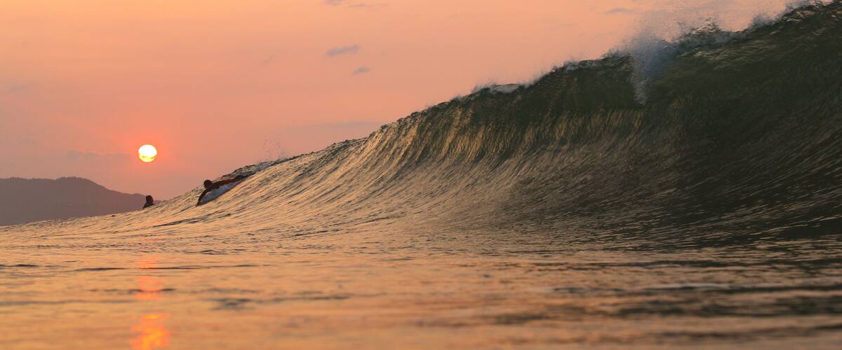 A large wave with a surfer riding it during sunset.