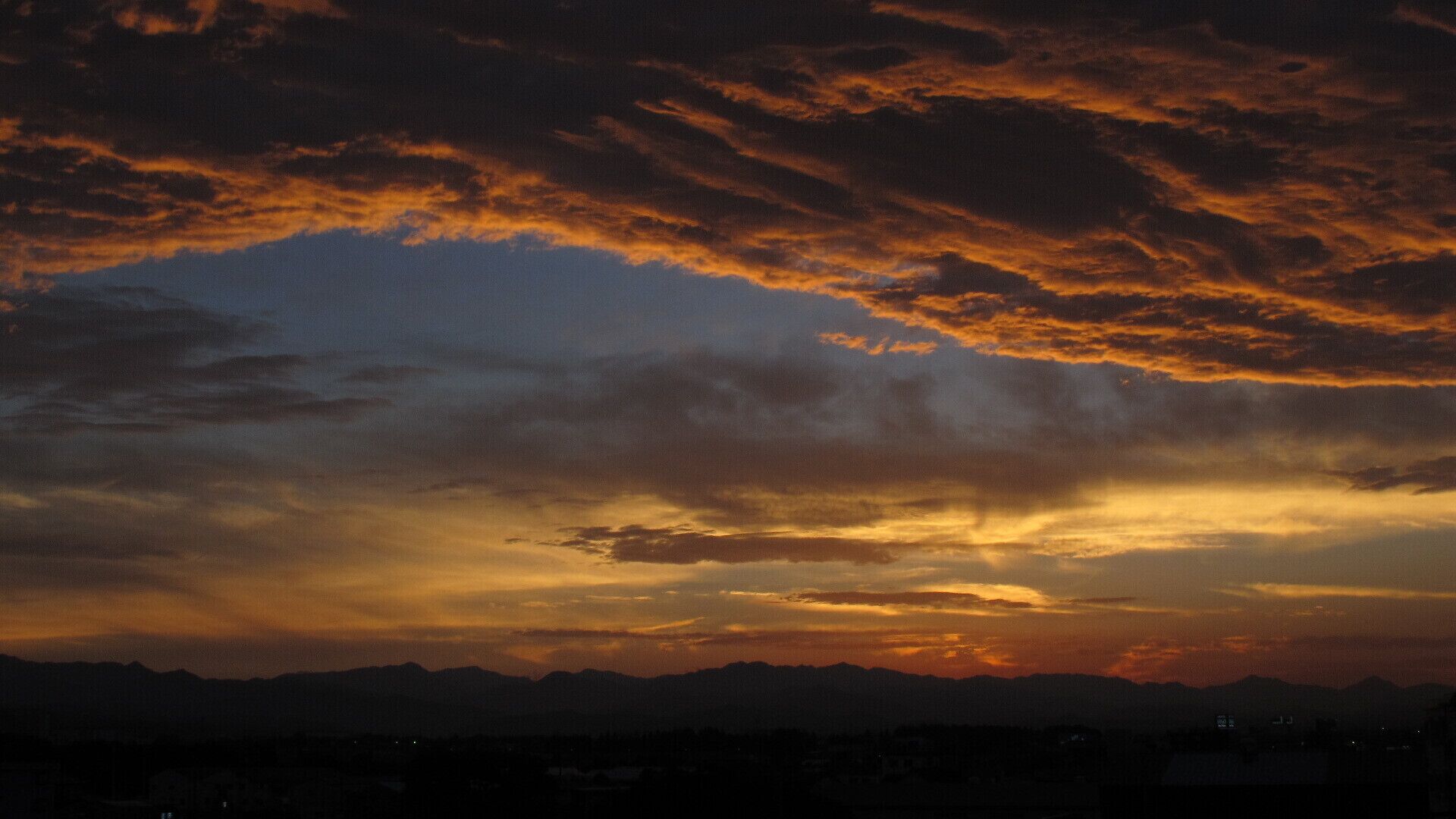 A sunset over a mountain range with a city in the foreground.