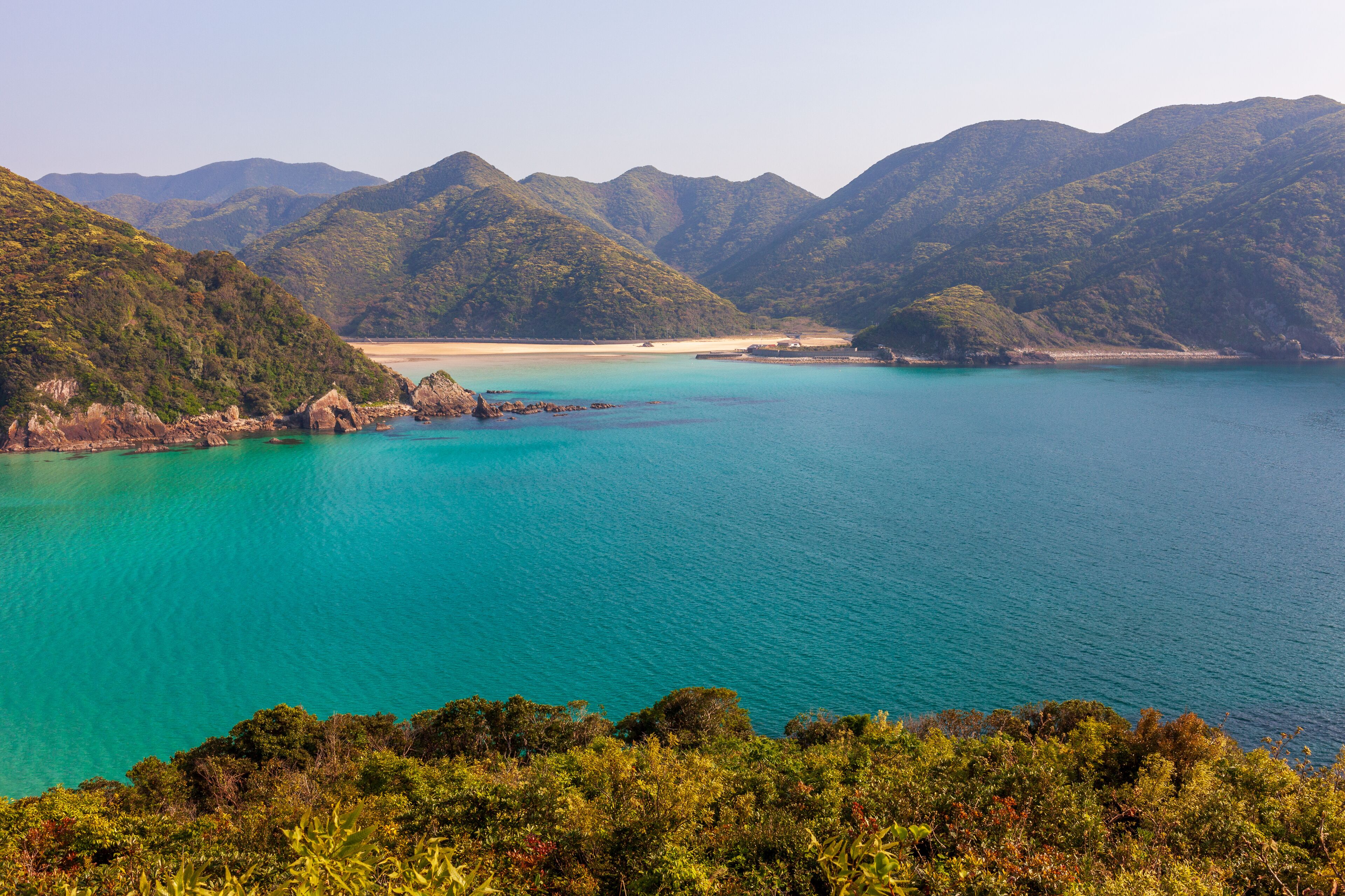 A coastal landscape with turquoise waters, green hills, and a sandy beach.