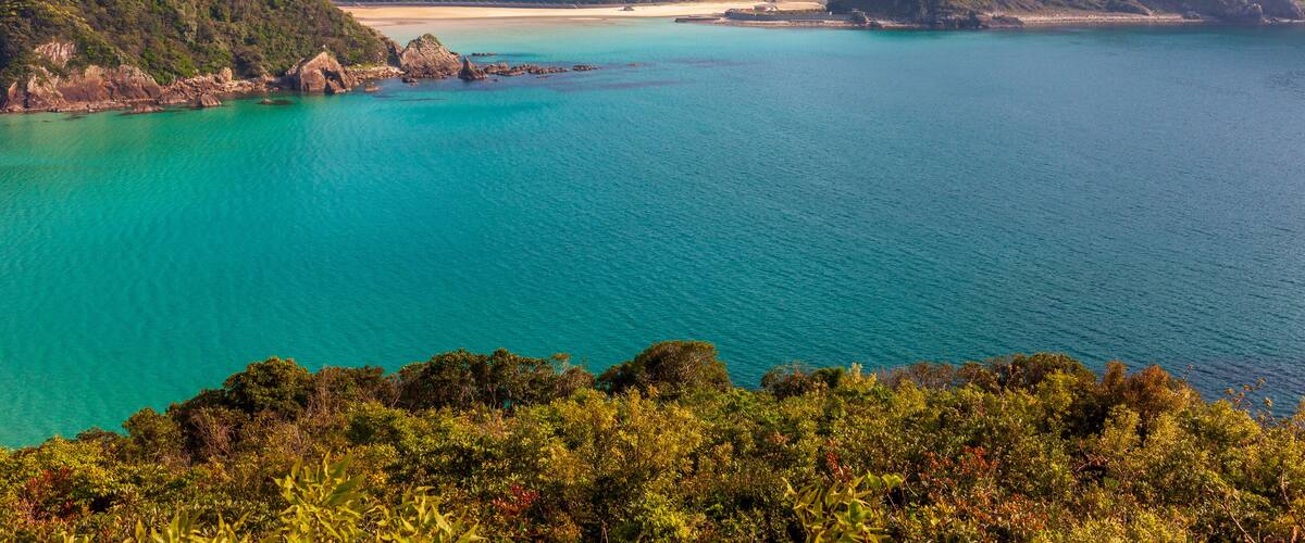 A coastal landscape with turquoise waters, green hills, and a sandy beach.