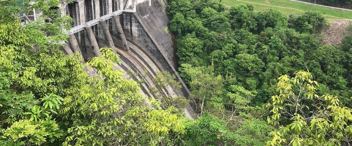 A large dam with multiple arches surrounded by dense forest.