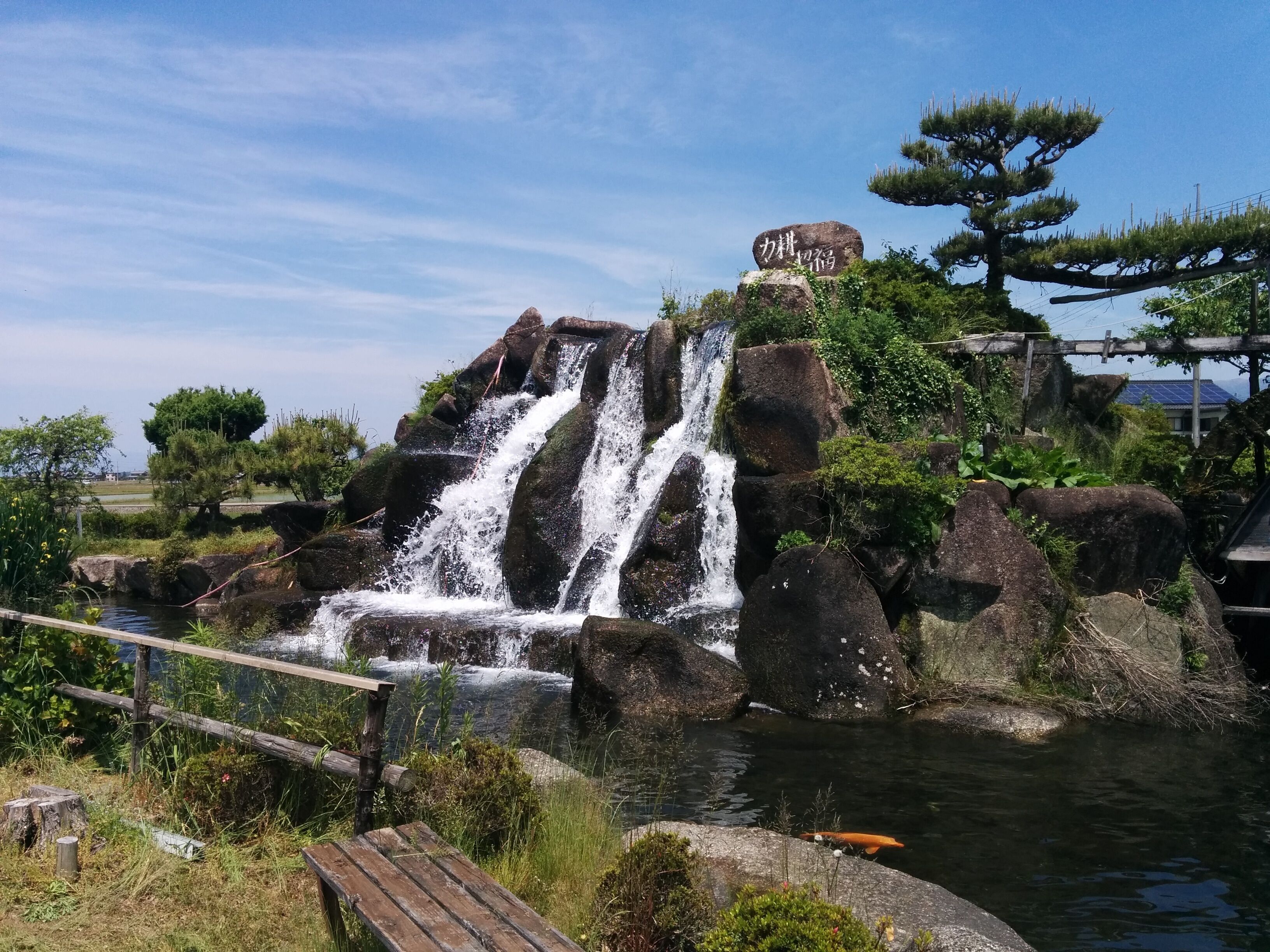 A waterfall cascading over rocks in a natural setting with a wooden bench and a sign.