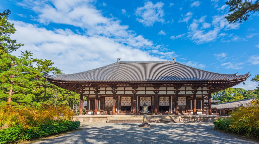 A traditional Japanese temple with a curved roof, wooden pillars, and a gravel path leading to the entrance.