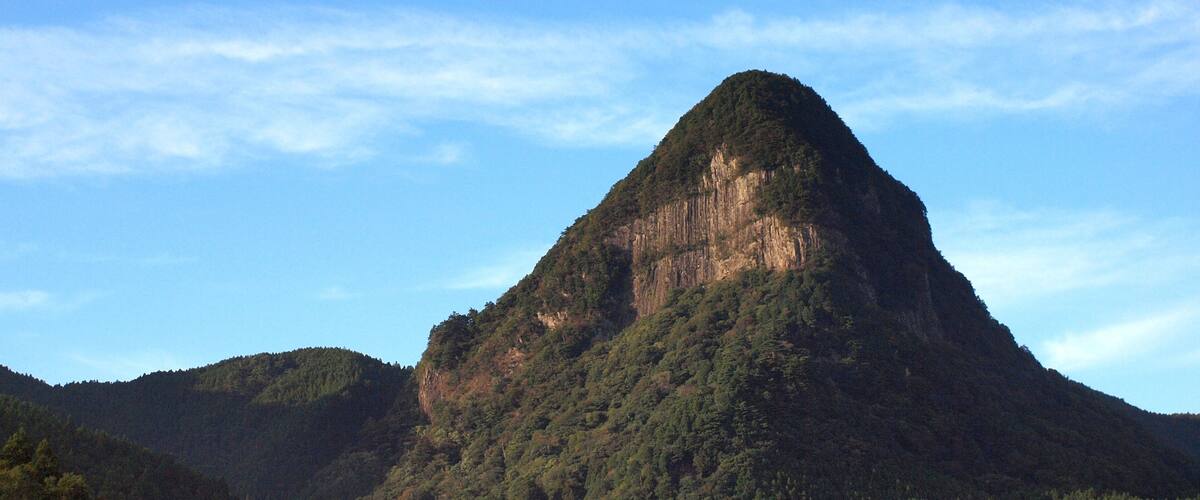 A mountain with a steep, forested peak and a clear sky.