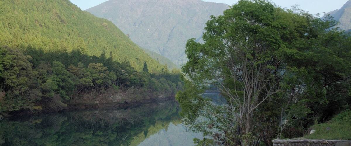 A calm lake reflecting the surrounding greenery and mountains.