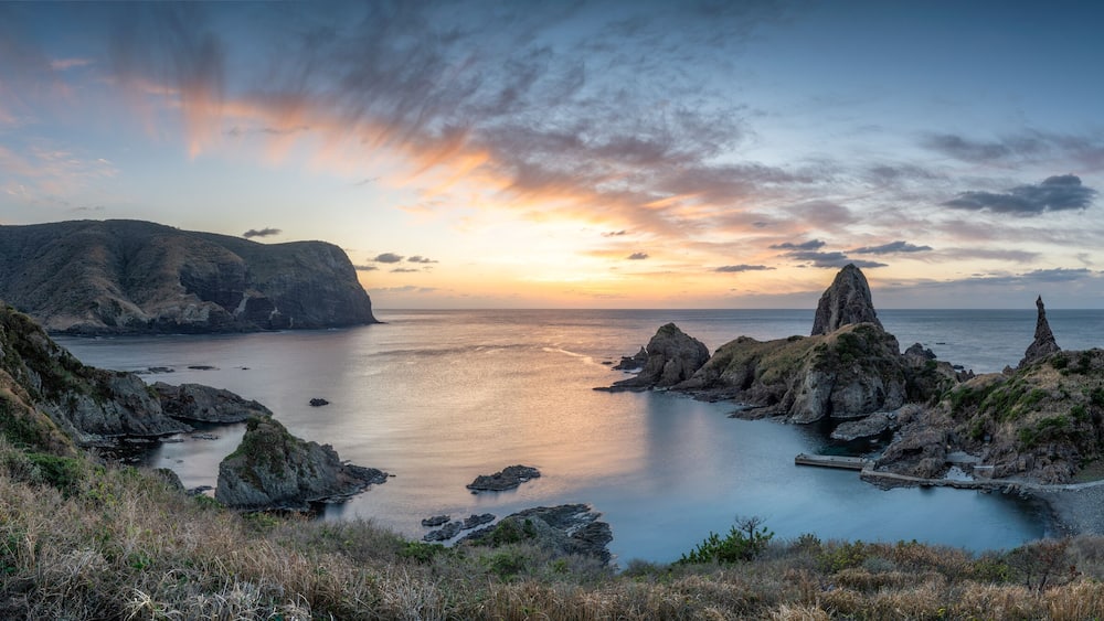 A coastal landscape with rocky formations and a calm sea at sunset.