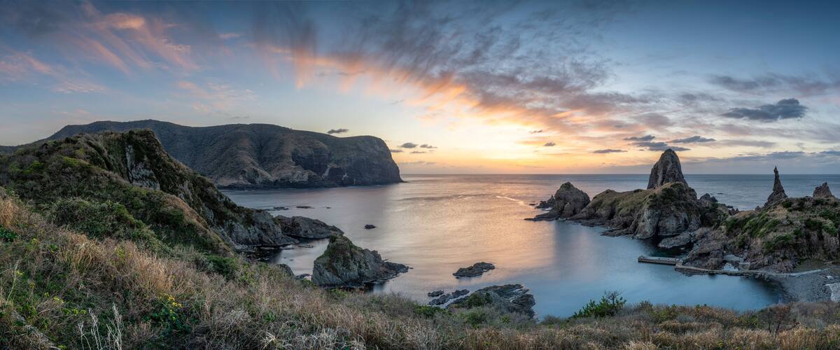 A coastal landscape with rocky formations and a calm sea at sunset.