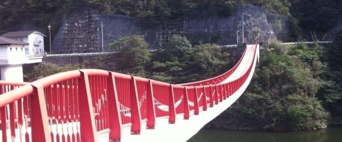 A red bridge over a river with a forested hillside in the background.