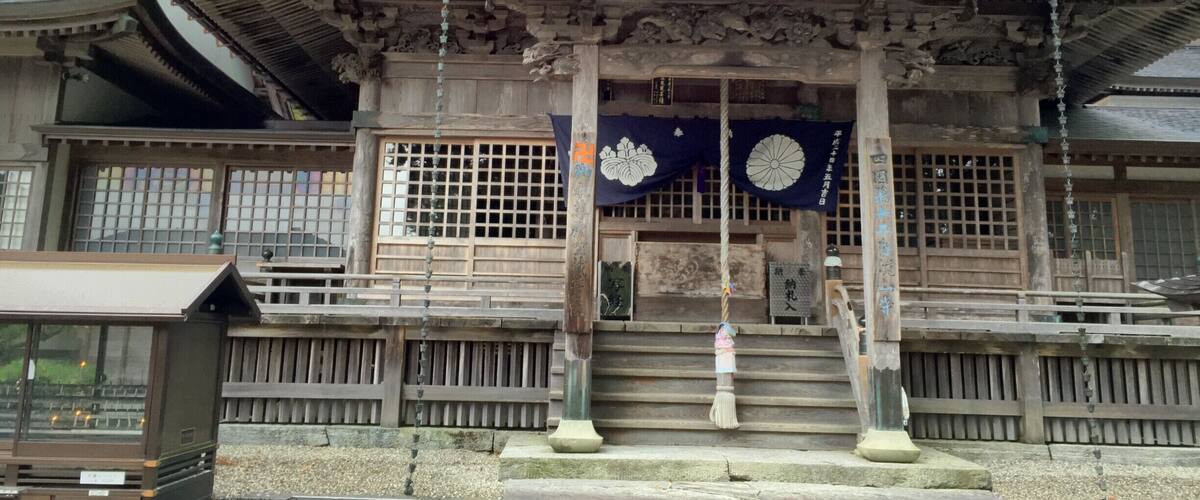 A traditional Japanese building with a curved roof, wooden lattice windows, and a stone staircase leading up to the entrance.