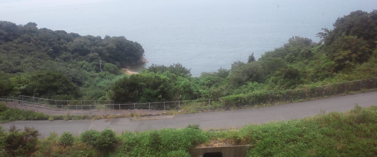 A coastal landscape with a road, dense greenery, and a calm sea with distant islands.