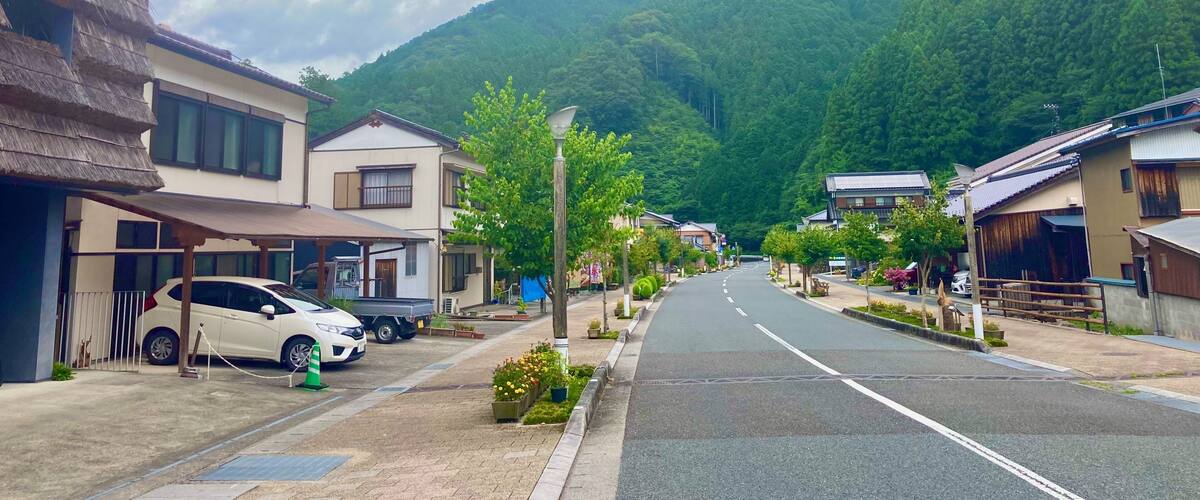 A street lined with traditional buildings, a parked car, and a mountain in the background.