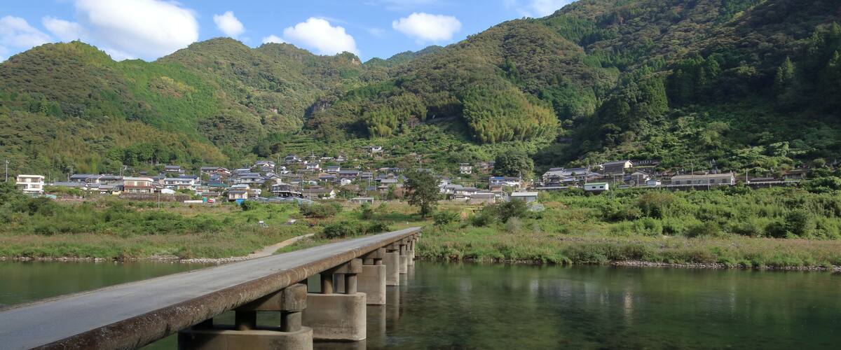 A bridge over a river with a town in the background and mountains.