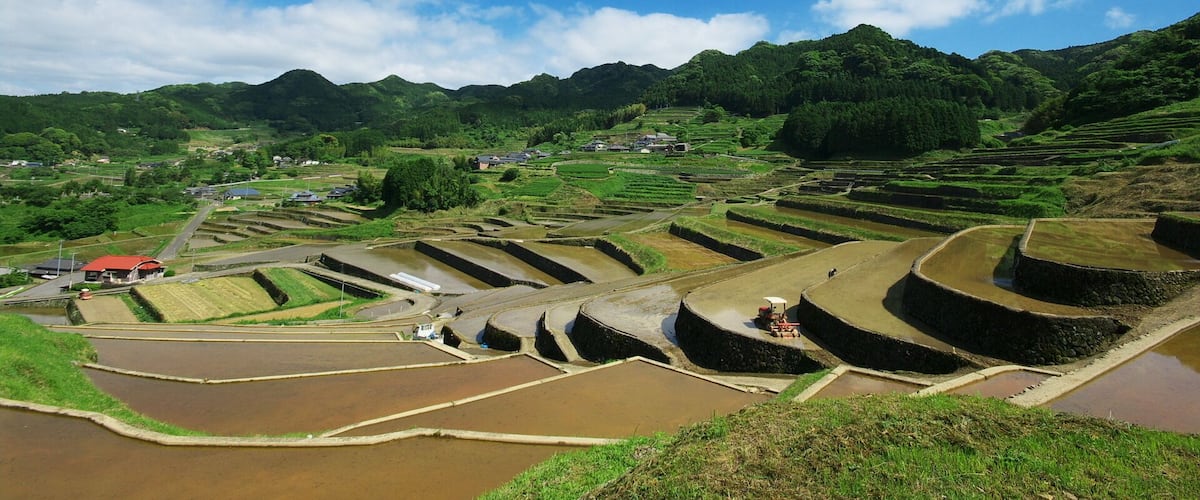 Terraced rice fields, a small village, and a mountain range under a clear blue sky.