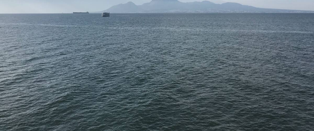 A calm sea with a small boat in the foreground and distant mountains under a cloudy sky.