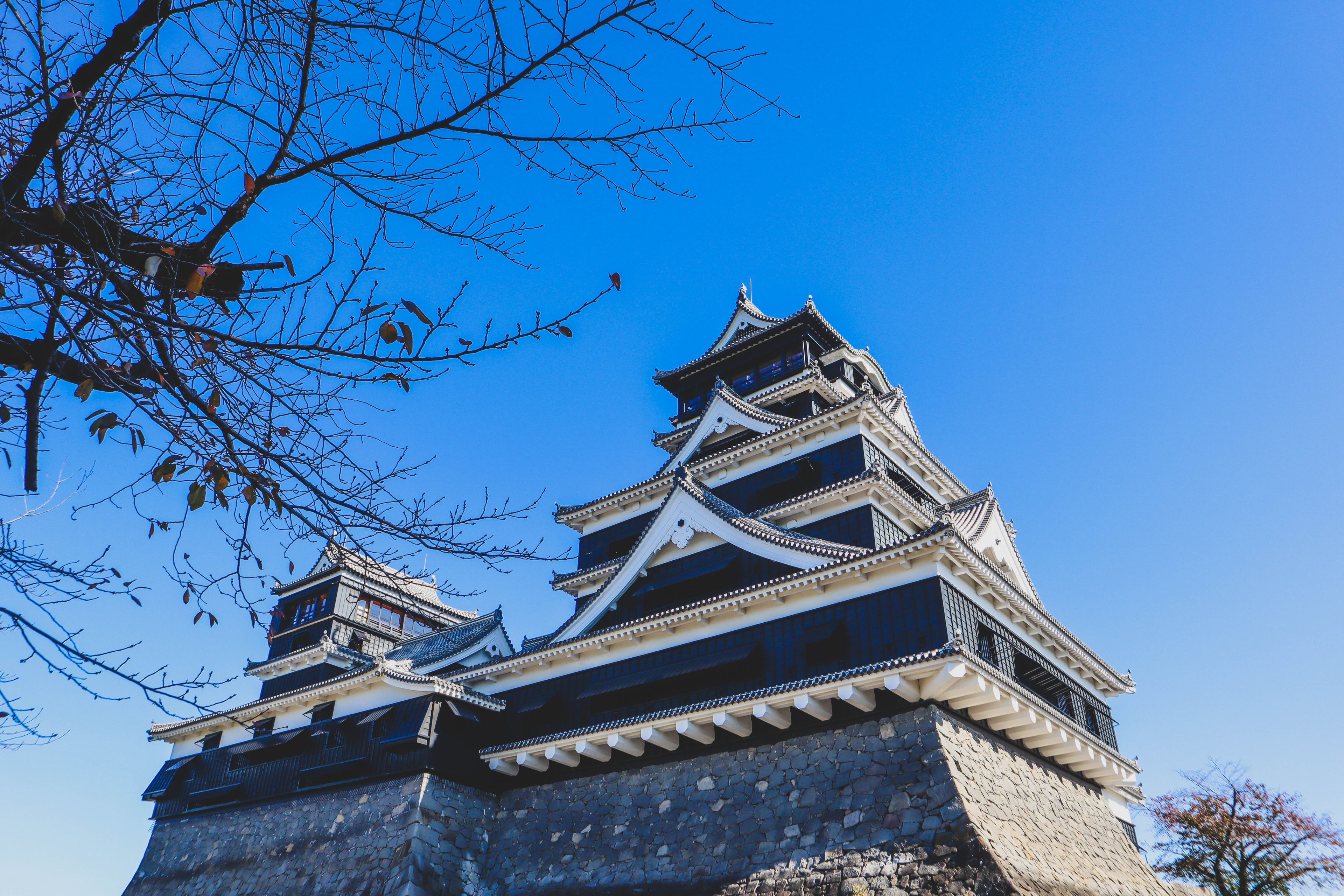 A traditional Japanese castle with multiple tiers and a stone base, set against a clear blue sky.