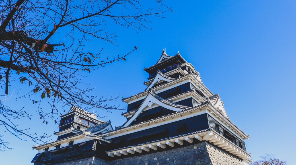 A traditional Japanese castle with multiple tiers and a stone base, set against a clear blue sky.