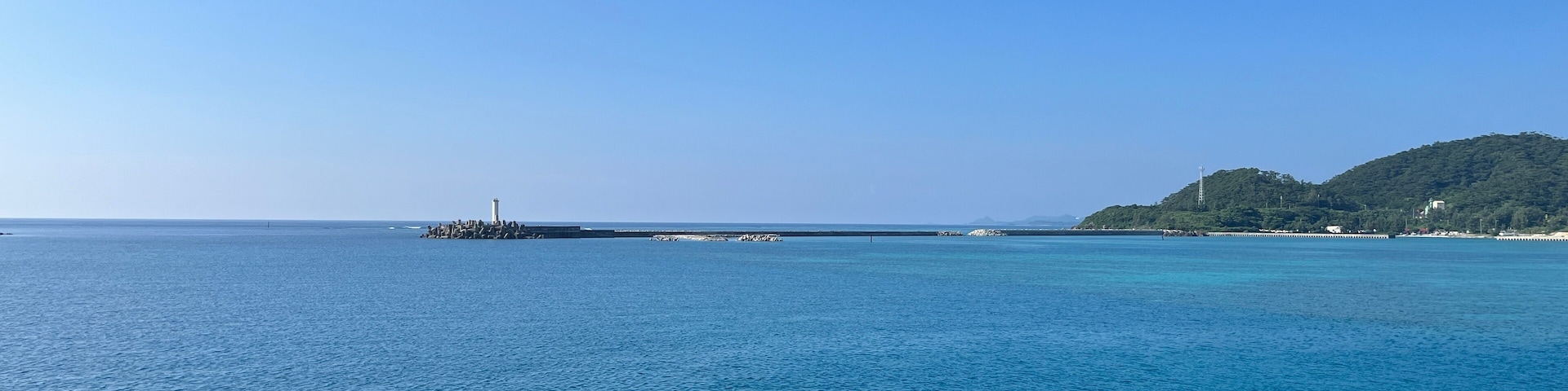 A calm sea with a lighthouse and a green hill in the distance.