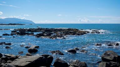 A rocky coastline with clear blue waters and distant mountains.