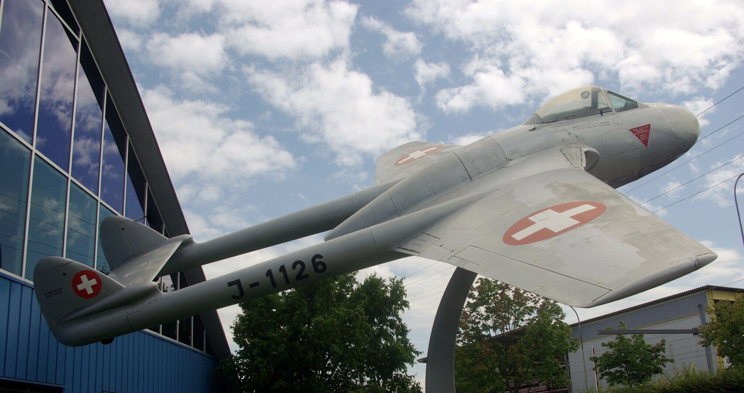 A vintage aircraft with a red cross emblem and the number J-1126, displayed outdoors.