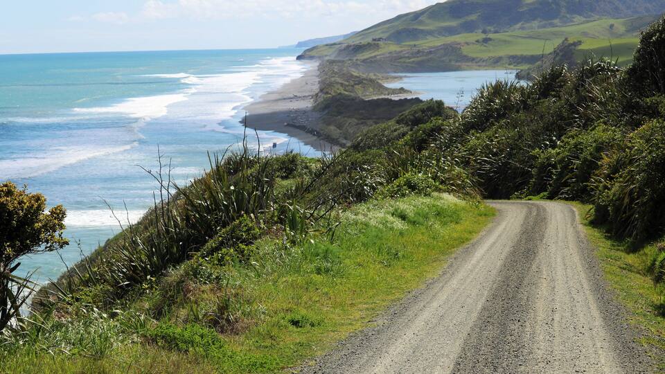 A coastal road with grassy hills and a beach.
