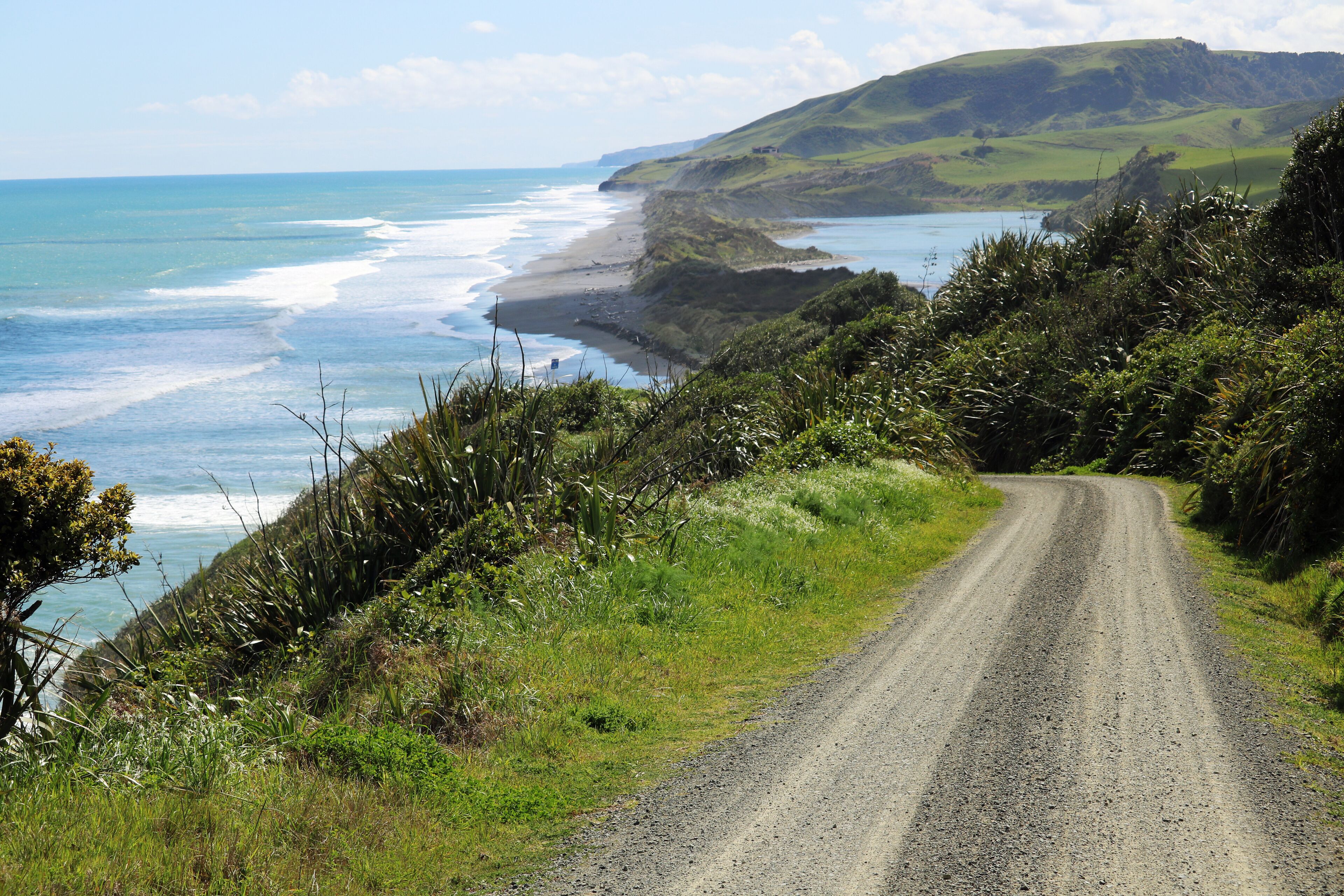 A coastal road with grassy hills and a beach.