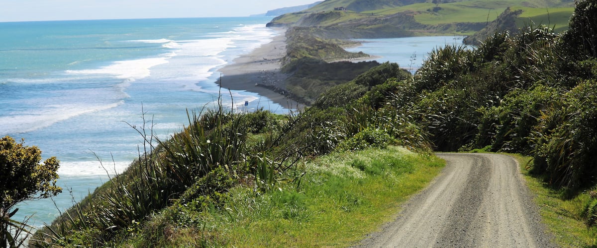 A coastal road with grassy hills and a beach.
