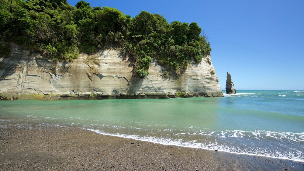 A coastal landscape with a prominent rock formation and a pebbly beach.