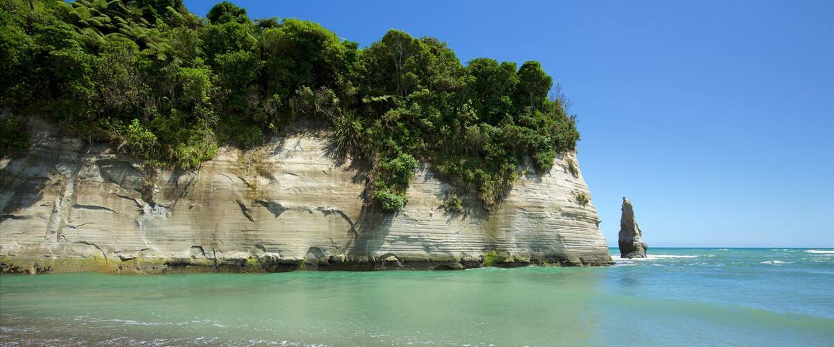 A coastal landscape with a prominent rock formation and a pebbly beach.