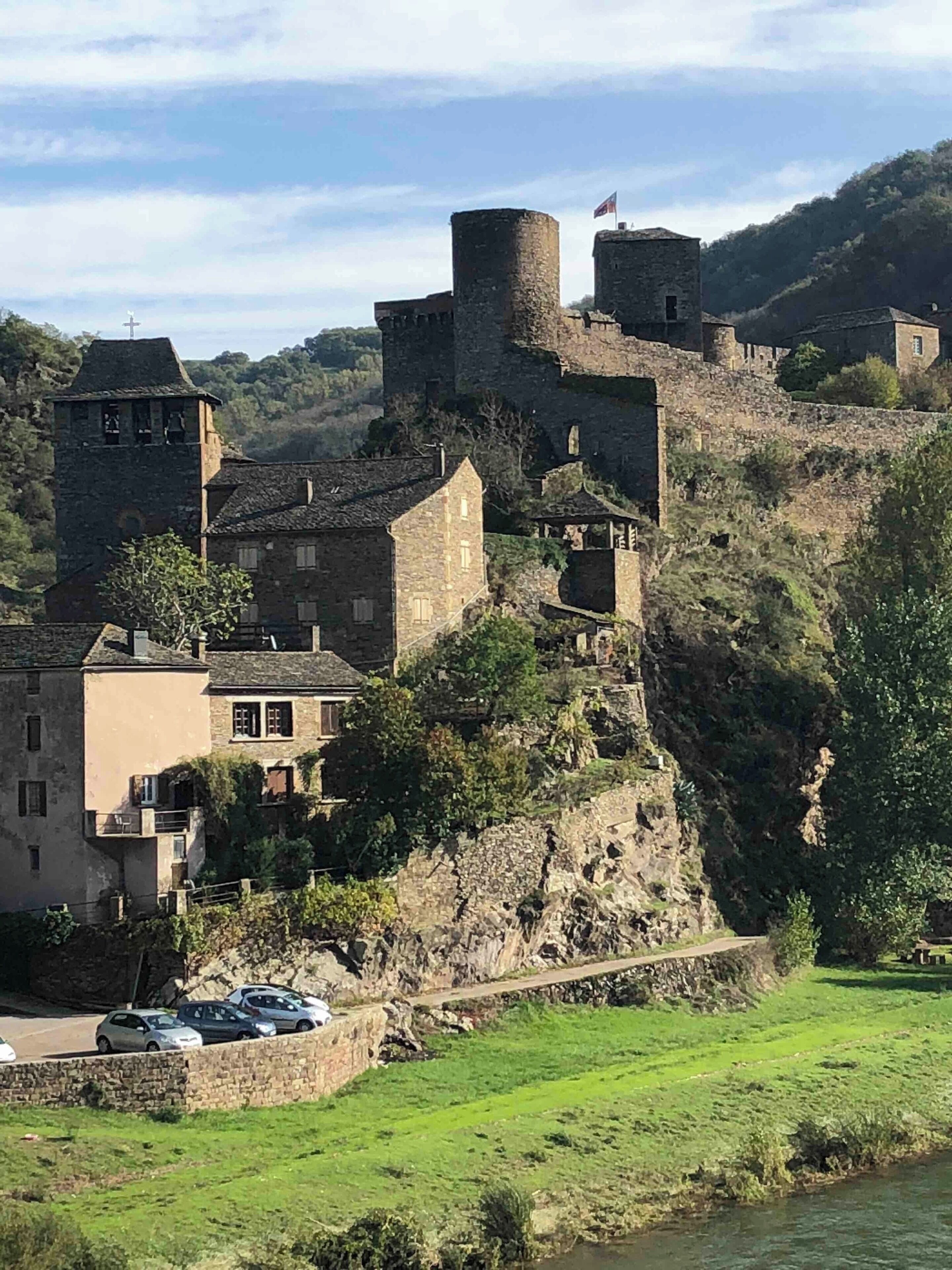 A medieval castle on a hillside with a river in the foreground.