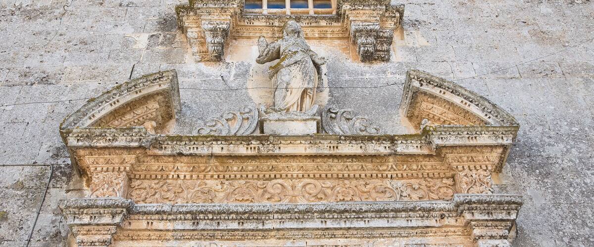 A detailed stone facade with a central statue, intricate carvings, and a wooden door.