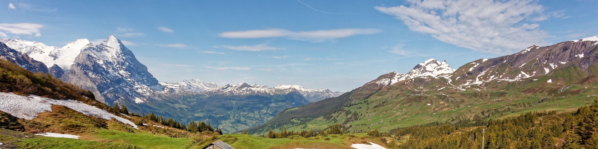 Un paisaje montañoso con picos nevados, una carretera sinuosa y casas de madera tradicionales.