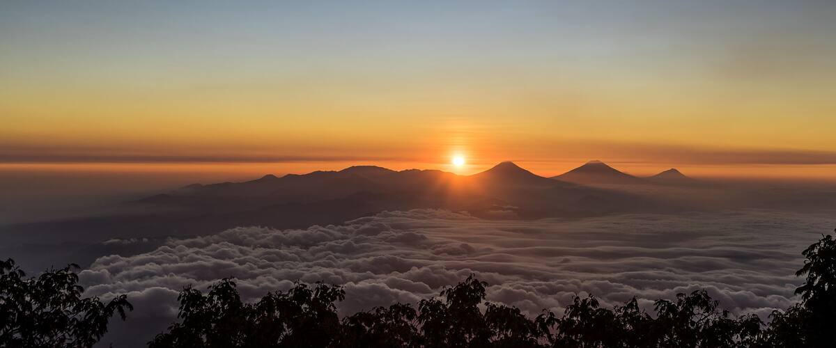 A sunrise over a mountain range with clouds below.