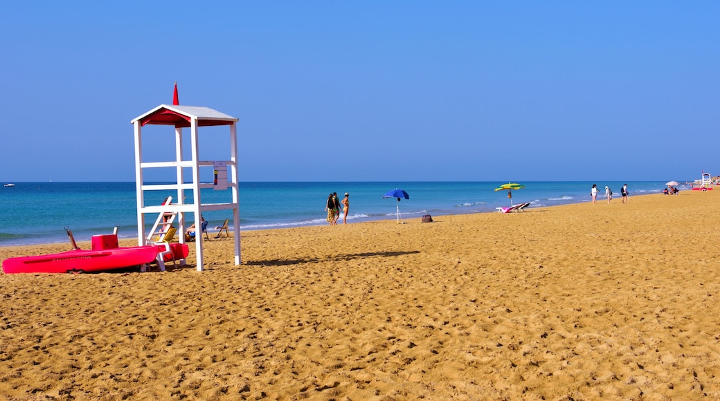 A sandy beach with a lifeguard tower, red lifeguard stand, and a few people in the distance.