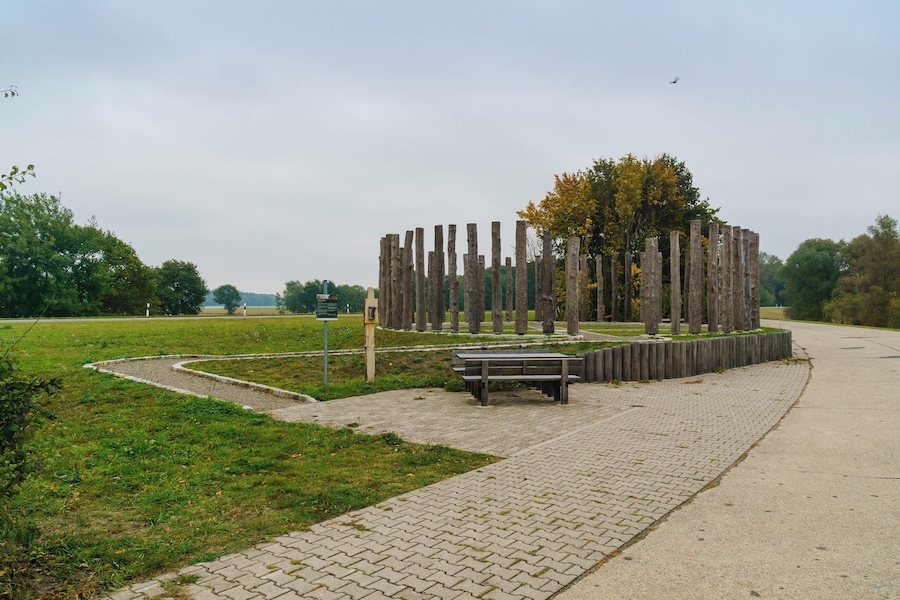 Un parque con una estructura de madera, un sendero pavimentado y un banco.