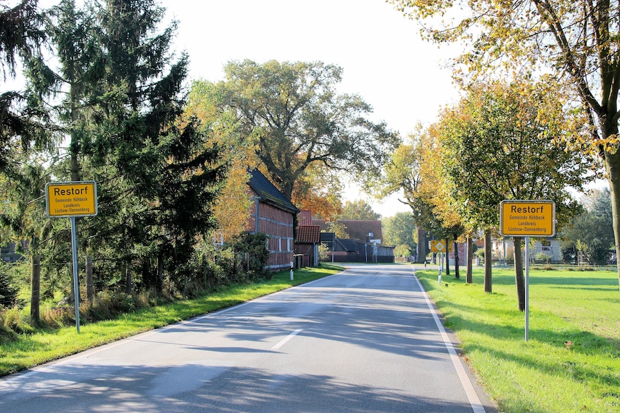 A road with two yellow signs indicating 'Restorf' and 'Luchow-Dannenberg'.