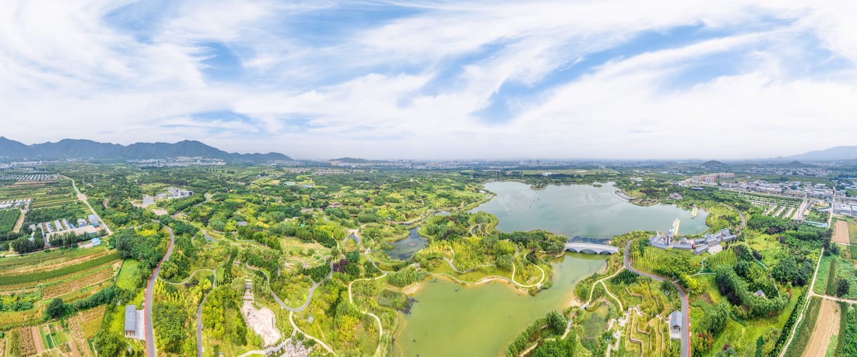 Une vue panoramique d’une ville avec un grand lac, des parcs verdoyants et des montagnes à l’horizon.